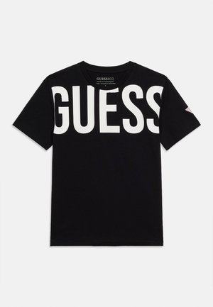 Svart T-skjorte med korte ermer, med stor hvit GUESS-logo over brystet og liten rød trekantet logo på venstre erme.