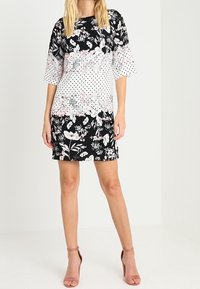 Květinové šaty s krátkými, rozšířenými rukávy. Černé pozadí s bílými puntíky a růžovými květy. Délka nad kolena, měkká látka. Růžové podpatky.