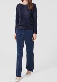 Marinrandig långärmad topp i kombination med marinblå manchesterbyxor och ljusa sneakers. Outfiten har en avslappnad passform och mjuk textur.