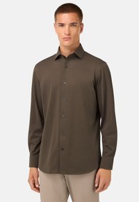 Brahns garais piedurkņu krekls mīkstā audumā, ar pogām uz apkakles un melnām pogām, veidots ar pieguļošu siluetu un gludu tekstūru.