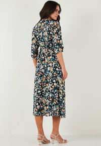Floral midi dress with a navy background, featuring orange and white flowers. Three-quarter sleeves and a tie waist detail. Soft fabric.