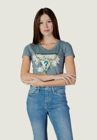 Svijetloplava majica s cvjetnim motivom i trokutastim dizajnom, u kombinaciji s visokim trapericama plave boje. Meko tkanje, kratki rukavi, okrugli izrez na vratu.