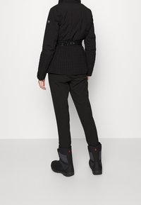 Black puffer jacket with a textured, quilted design and belted waist. Paired with black pants and waterproof black boots with pink accents.