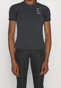 Camiseta deportiva gris oscuro de manga corta, con acentos texturizados en los hombros y el logo de Nike impreso en el pecho. Material liso y ajustado.