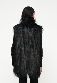 Colete de pelo falso preto com fibras longas e direitas e uma gola alta. A parte de trás apresenta um design em camadas, contrastando com a frente lisa e ajustada.