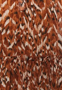 Tissu imprimé animalier marron, noir et blanc avec un détail de couture froncée et une petite boucle en tissu près du centre supérieur.