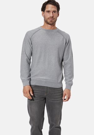 Grauer Pullover aus weicher Stoffqualität, mit klassischem Rundhalsausschnitt und gerippten Bündchen, kombiniert mit dunkelgrauen Jeans.
