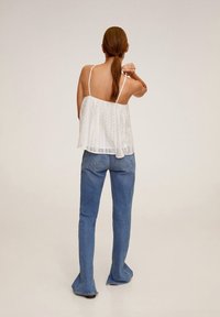 Haut blanc sans manches avec des détails semblables à de la dentelle, associé à un jean évasé bleu clair. Le haut est ample et présente un dos échancré.