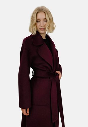 Burgunderfarget innpakningsfrakk med stor krage, lange ermer, beltedetalj og sidelommer. Laget av et mykt, strukturert stoff.