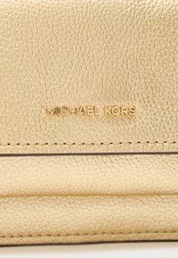 Portofel din piele texturată aurie, cu inscripția „MICHAEL KORS” în relief auriu, având cusături detaliate pe margini și un design elegant, minimalist.