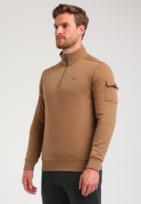 Bruine half-zip pullover gemaakt van textuurstof, met een borstzak met knoopsluiting en geribde manchetten. Casual ontwerp.