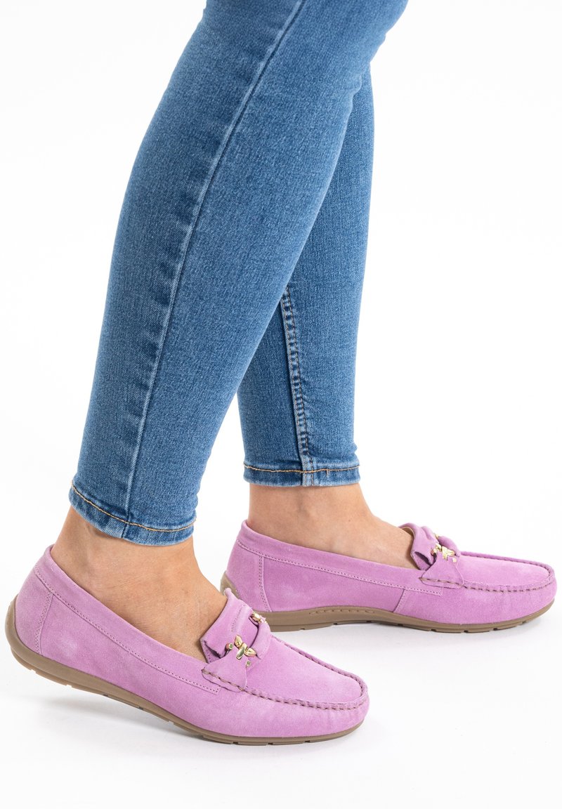Light purple suede moccasin shoes with a rounded toe, gold hardware accents, and a flexible beige sole, worn with blue skinny jeans.