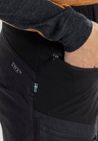 Zwarte SWYX™ pants hebben een ritszak, een accent van de Zweedse vlag en een combinatie van gestructureerde en gladde stoffenpanelen.