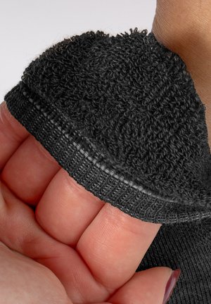 Dłoń wsuwająca się do czarnej rękawiczki bez palców z teksturowanej dzianiny i elastycznym mankietem na nadgarstku na jasnym tle.