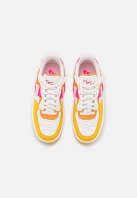 Paire de baskets blanches avec des accents jaunes, roses et orange, lacets blancs et bouts perforés, vues de dessus sur un fond blanc.