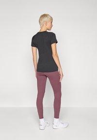 Tmavě šedý top s krátkým rukávem, který je zkombinován s těsnými, růžovofialovými legínami. Modelka má na sobě bílé tenisky, které mají jednoduchý sportovní design.