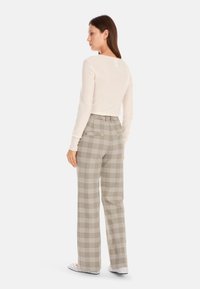 Long-sleeve beige top paired with high-waisted plaid trousers in grey and cream, featuring a relaxed fit and back pockets.