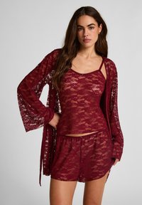 Σετ νυχτικά από μπορντό δαντέλα που περιλαμβάνει τοπ με λεπτές τιράντες και κοντό σορτς, με απαλό, διαφανές ύφασμα και λουλουδένιο σχέδιο.