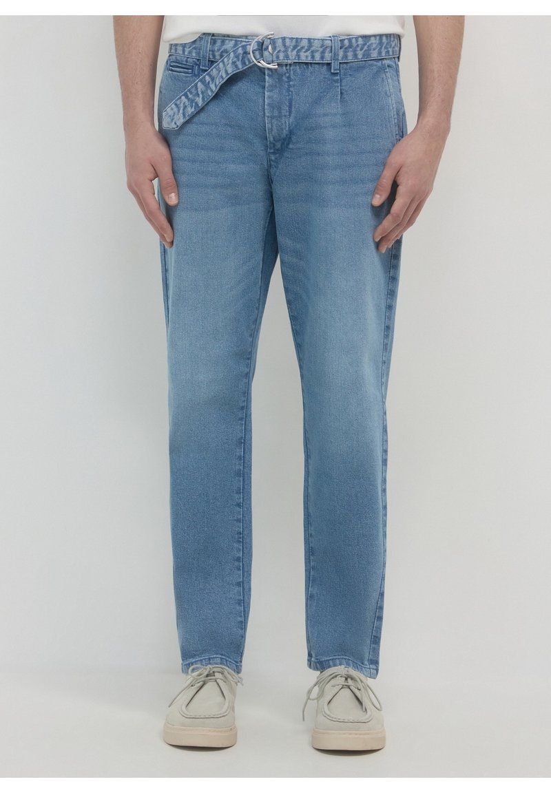 Jeans en denim bleu clair avec une coupe à jambe droite, dotés d'une ceinture à motifs et de détails de surpiqûres visibles. Portés avec des chaussures gris clair.