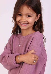 Le set de bijoux en argent comprend un collier, un bracelet et des boucles d'oreilles avec de petits détails en charme. L'enfant porte un pull rose texturé.