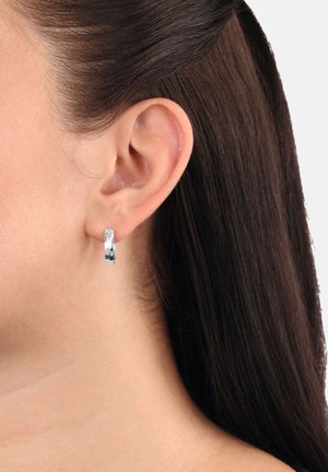 Pendiente de aro de metal plateado que exhibe una superficie lisa y pulida, con un diseño circular; cuenta con un cierre seguro en la parte posterior.