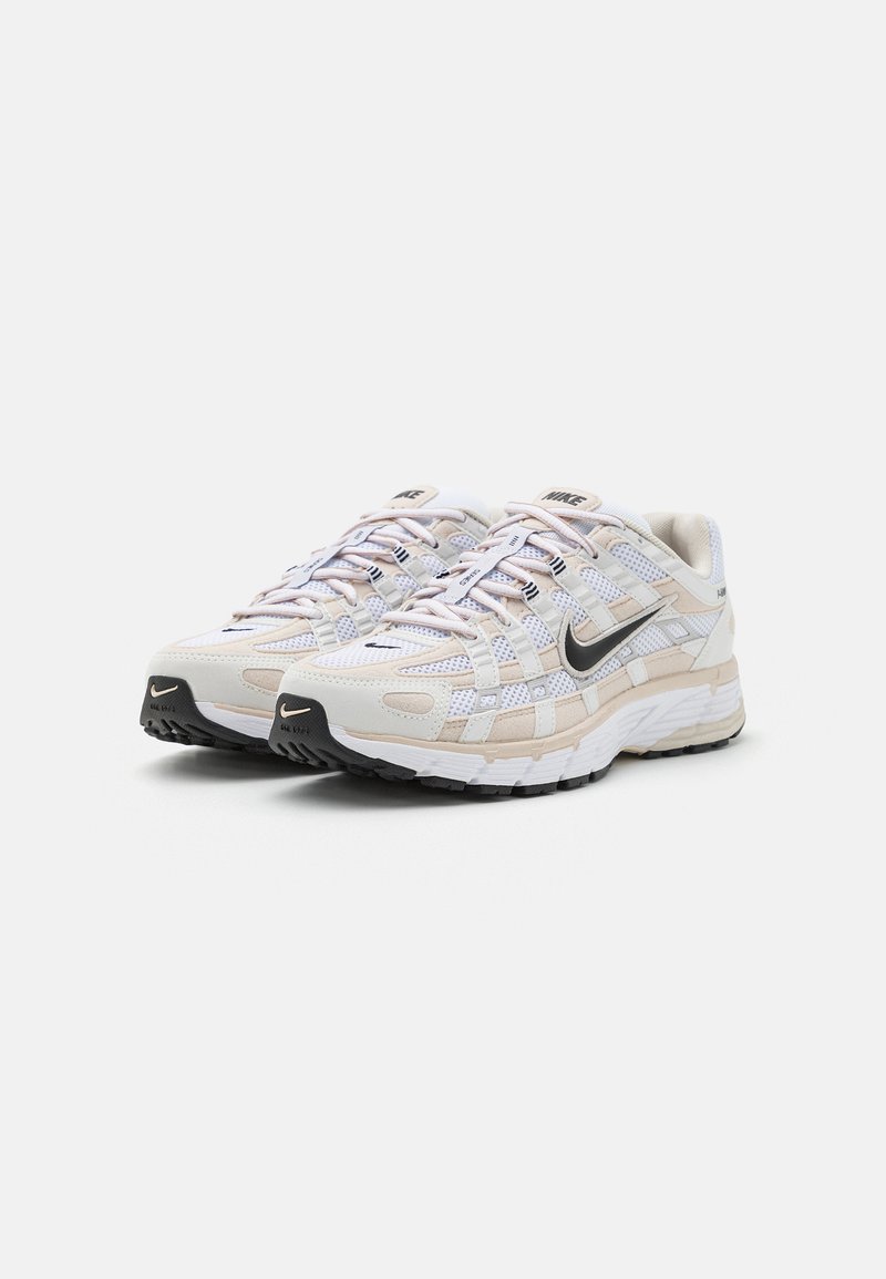 Weiße Sportschuhe mit einem Obermaterial aus Mesh und Synthetik, schwarzem Nike-Swoosh, beigen Akzenten und einer strukturierten, schwarzen Sohle. Schnürdesign.