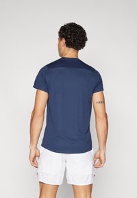 T-shirt atlético azul marinho com mangas curtas, design ajustado e textura suave. Usado com calções brancos, mostrando uma silhueta simples e moderna.