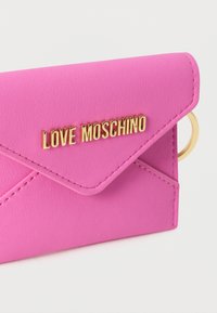 Καπιτονέ ροζ πορτοφόλι από ψεύτικο δέρμα με καπάκι φάκελο, διακοσμημένο με χρυσό λογότυπο "LOVE MOSCHINO" και μεταλλικό μπρελόκ σε χρυσό χρώμα.