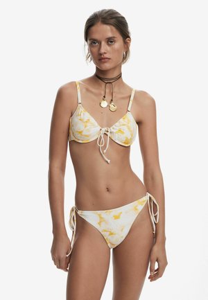 Bikini set featuring a white fabric with yellow leaf patterns, adjustable tie strings on both top and bottoms, and thin shoulder straps.