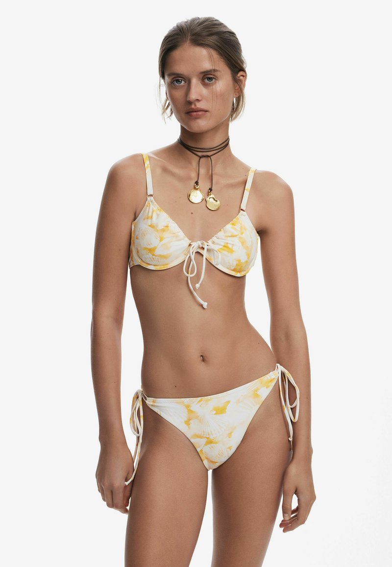 Bikini-set met een witte stof met gele bladerenpatronen, verstelbare strikjes aan zowel de boven- als onderkant, en dunne schouderbanden.