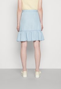 Saia de ganga azul clara com uma bainha franzida e uma cintura ajustada, apresentando uma textura suave e um design simples. Usada com calçado claro.