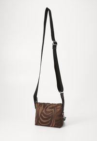 Brown crossbody bag made of fabric with a textured, abstract wave pattern. Features a black adjustable strap and silver hardware accents.