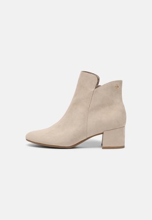 Beiger Wildleder-Stiefelette mit Blockabsatz, spitzer Zehenpartie und Logodetail an der Seite vor weißem Hintergrund.