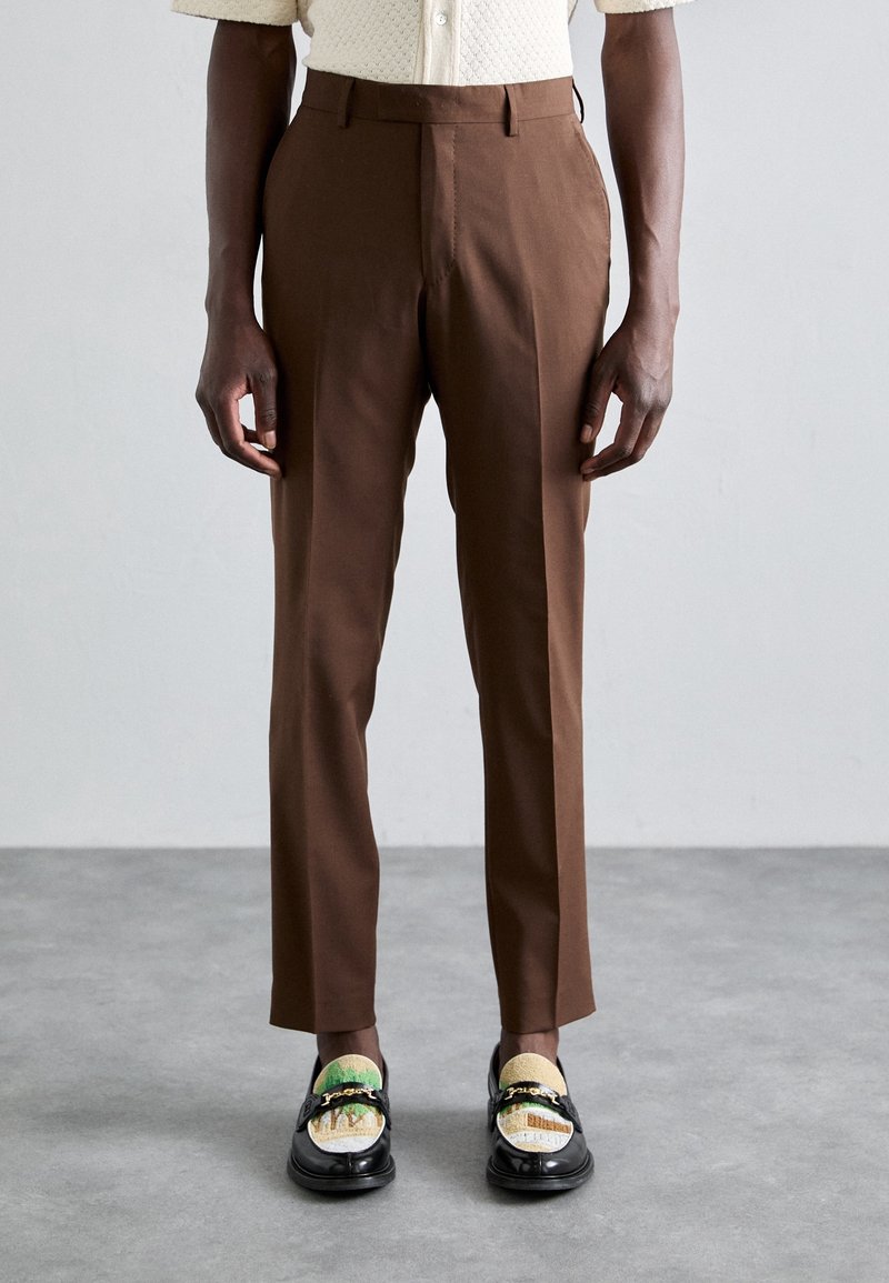 Bruna skräddarsydda byxor med en slät yta, med rak passform, bältesöglor och minimal sömnadsdetalj, i kombination med mönstrade loafers.