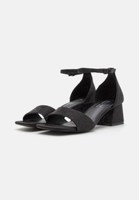 Sandales à talons noirs avec un dessus texturé, une large lanière, un open toe et une lanière de cheville. Design à talon carré pour plus de stabilité.