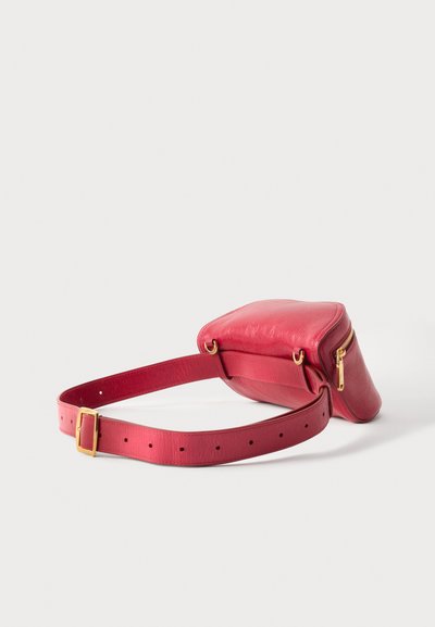 Κόκκινο δερμάτινο τσαντάκι μέσης με χρυστό φερμουάρ και ρυθμιζόμενο λουράκι, εμφανίζεται σε ανοιχτό γκρι φόντο.