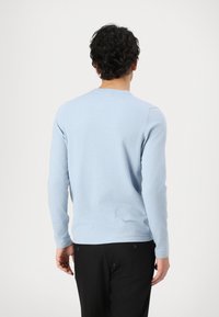 Helles blaugraues Langarmshirt aus weichem Material, mit Rundhalsausschnitt und dezentem Muster, kombiniert mit schwarzen Hosen.