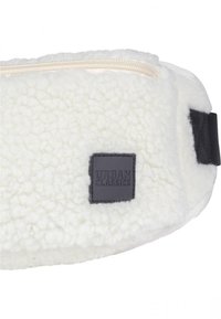 Hvit fleece bag med en myk tekstur, med en beige glidelås, svarte stoffdetaljer og en svart firkantet etikett med "URBAN CLASSICS" preget.