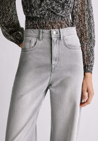 Svijetlosive traperice visokog struka, s prednjim džepovima, zatvaranjem na gumb i ravnim krojem za ležeran izgled.