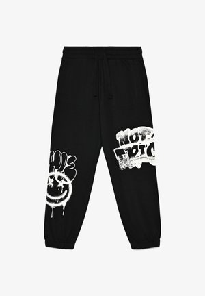 Pantaloni della tuta neri con disegni grafici bianchi, inclusi un volto sorridente e testo, vita con coulisse e polsini a costine.