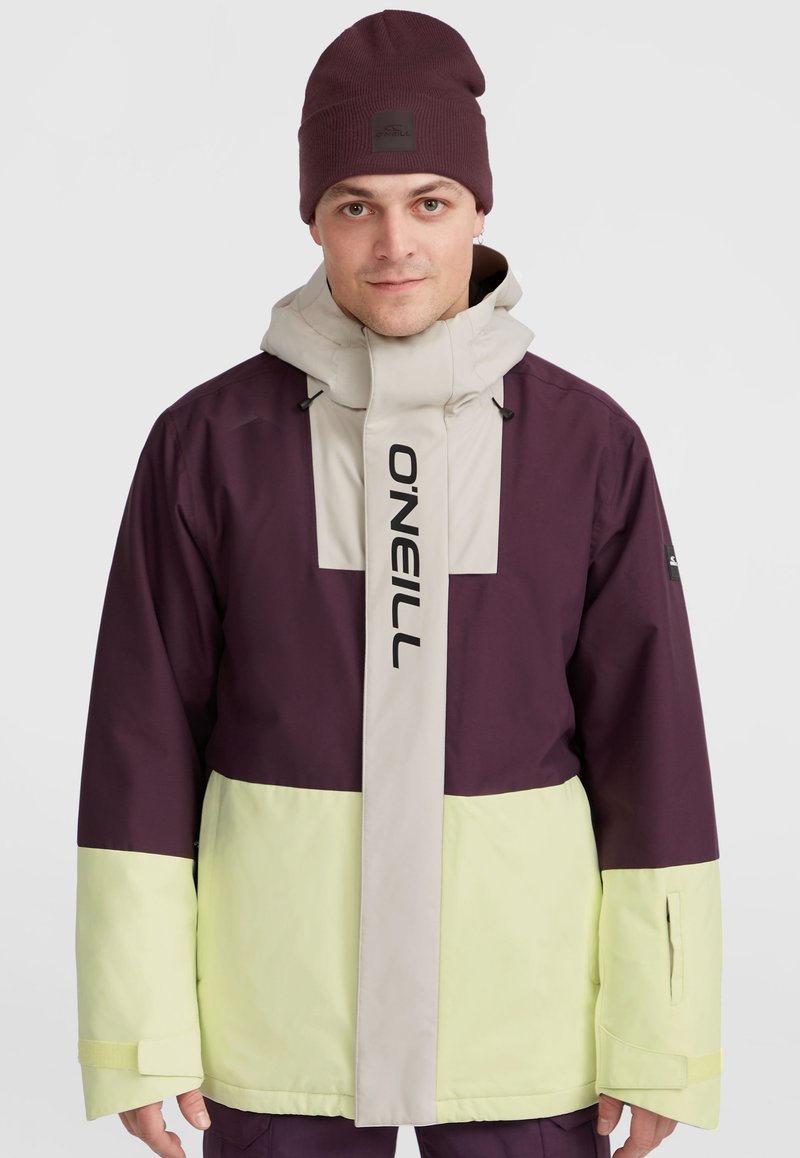 Lila und hellgrüne Jacke mit hohem Kragen, verstellbarem Kapuzen und Logo auf der Vorderseite. Glattes Material mit kontrastierenden Farbblöcken.