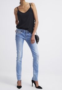 Černá saténová košile, světle modré džínsy skinny, černé špičaté podpatky a malá černá kabelka přes rameno. Minimalistický design, hladká textura.