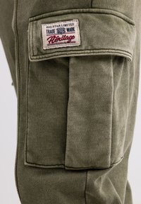 Pantaloni cargo verde oliva in tessuto con finitura testurizzata, caratterizzati da un'etichetta a patch evidente che reca la scritta "BIG STAR LIMITED" e una grande tasca laterale.