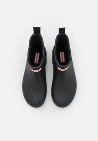 Bottines noires en caoutchouc avec une finition texturée, dotées d'une languette et d'une étiquette logo blanche et rouge sur le côté.