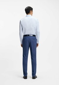 Camicia a quadretti azzurri con maniche lunghe, abbinata a pantaloni sartoriali blu scuro e cintura nera. Tessuto liscio, design formale.