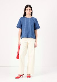 Top in denim con strisce bianche verticali, maniche corte e scollatura rotonda. Abbinato a pantaloni larghi color crema e scarpe rosse con tacco alto.