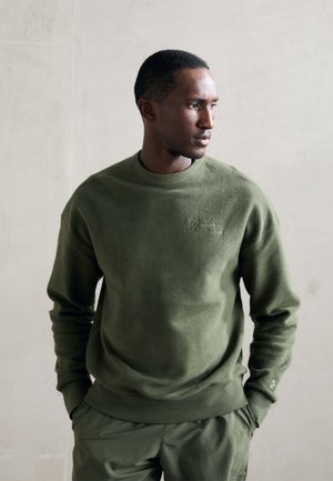 Green knitted sweatshirt with a round neckline and textured fabric. Features subtle embroidery and ribbed cuffs, paired with matching pants.