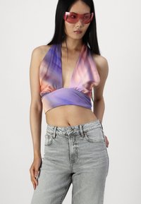 Kratka majica s halter vratom v tkanini z vijoličnim in breskovim gradientom, v kombinaciji z visokim pasom svetlo sivoh jeans. Ima zasnovo z zbranim pasom.