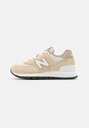 Beżowo-białe buty sportowe New Balance z zamszowymi i siateczkowymi detalami, biała śródpodeszwa i czarna podeszwa zewnętrzna widziane z boku.