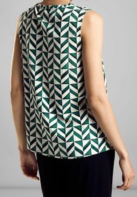 Ärmlös topp med ett geometriskt mönster i grönt och vitt. Slättyg med rundad halsringning och subtila rynkor bak.
